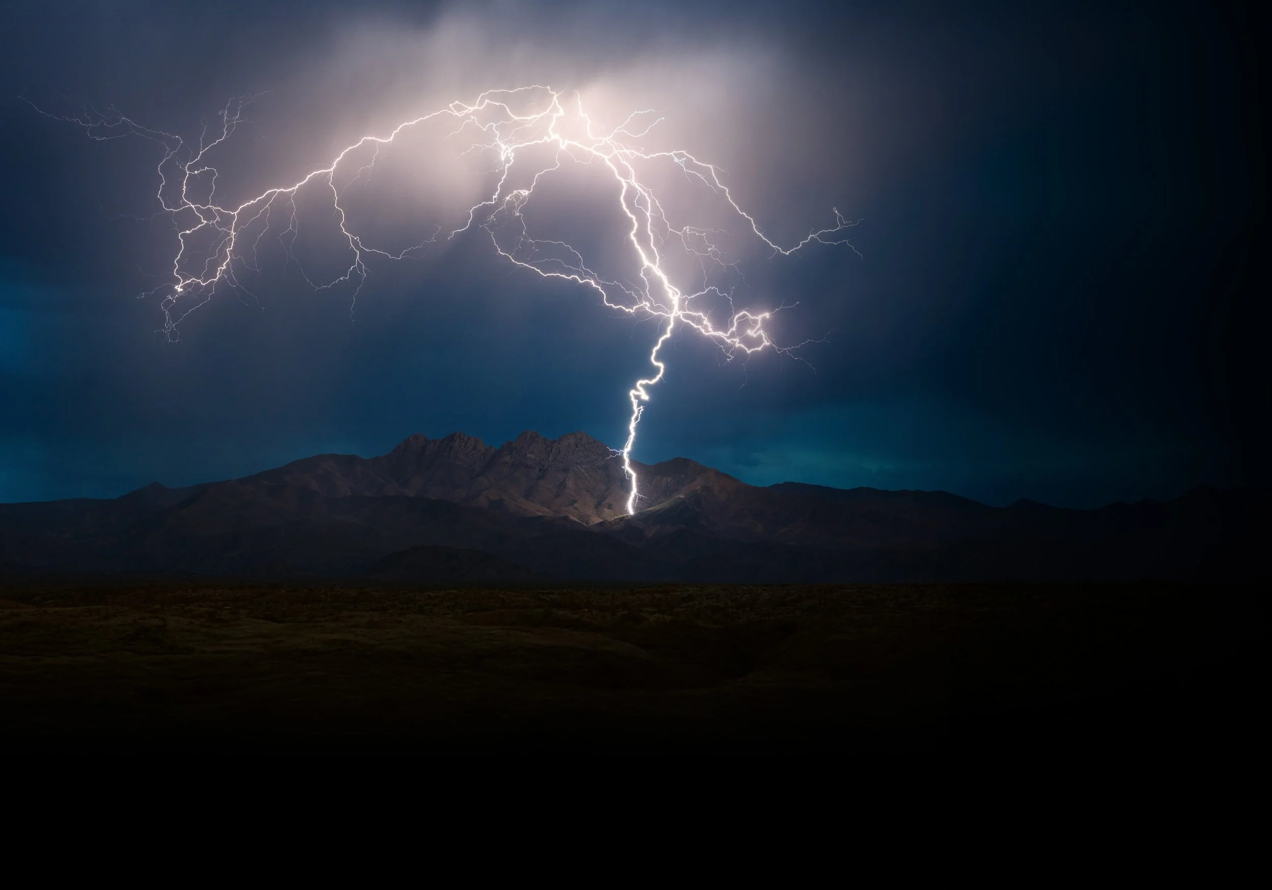 A lightning storm over a mountain landscape at night, with multiple lightning bolts striking from dark clouds.