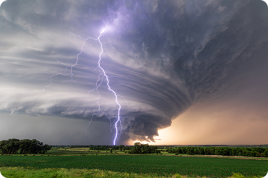 Lightning bolt strikes sky over a stormy landscape with clouds and farmland at sunset.