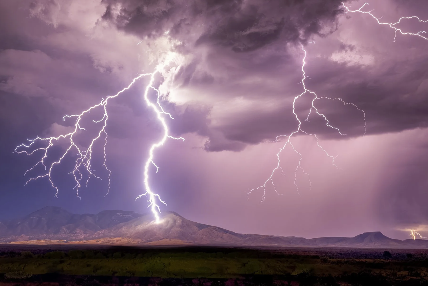 Lightning strikes over a mountain range during a thunderstorm at dusk.