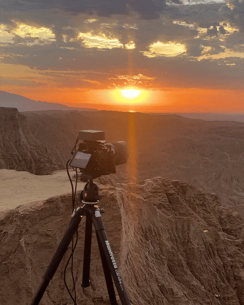Camera on a tripod capturing a sunset over rugged mountains and canyons.