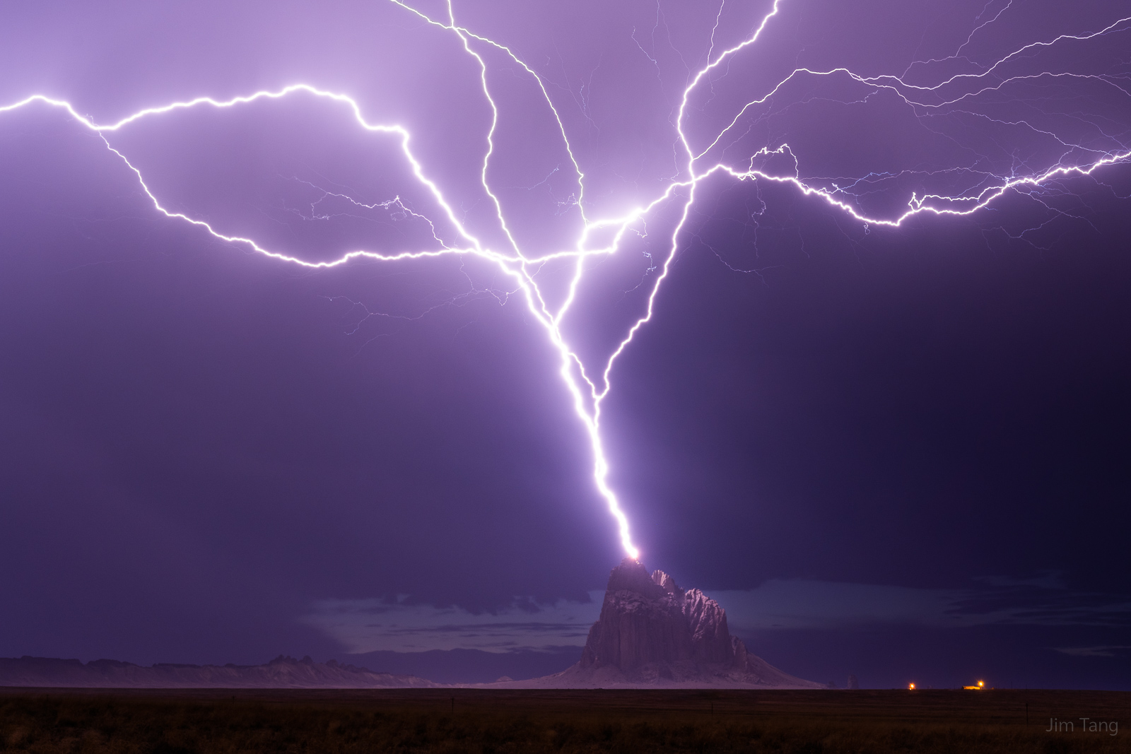 Lightning strike hitting a mountain in a desert landscape at night with dark clouds
