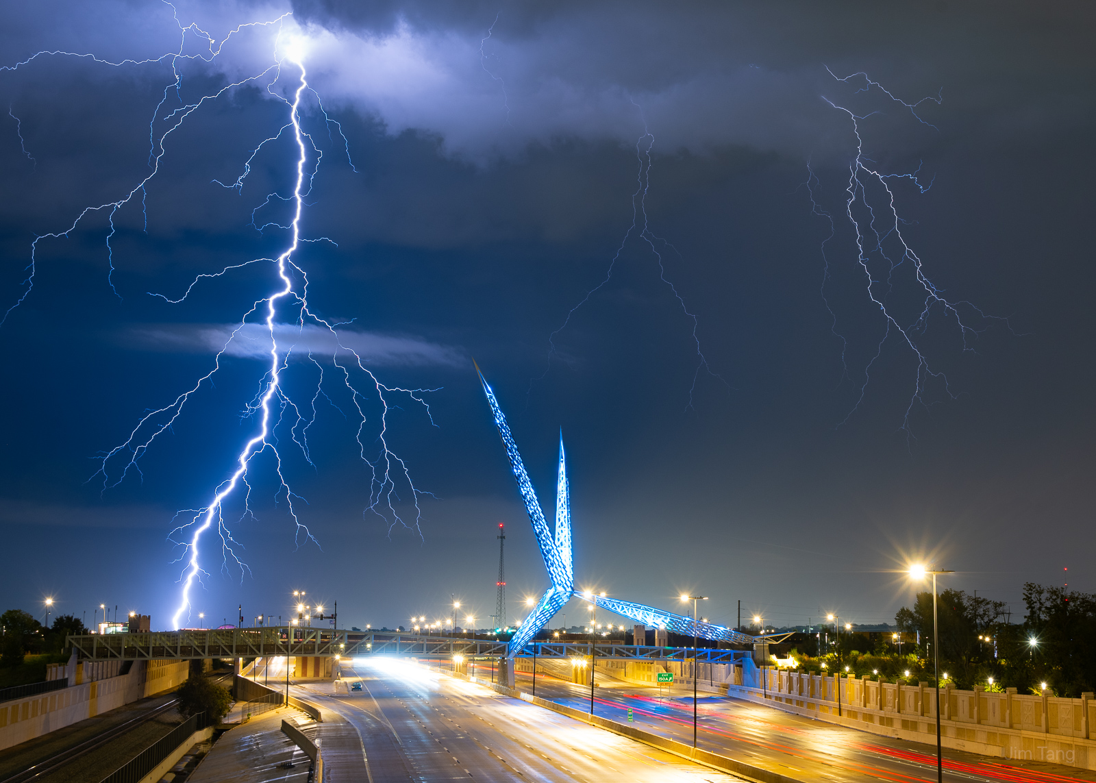 Lightning storm over a highway with a blue sculpture and streetlights