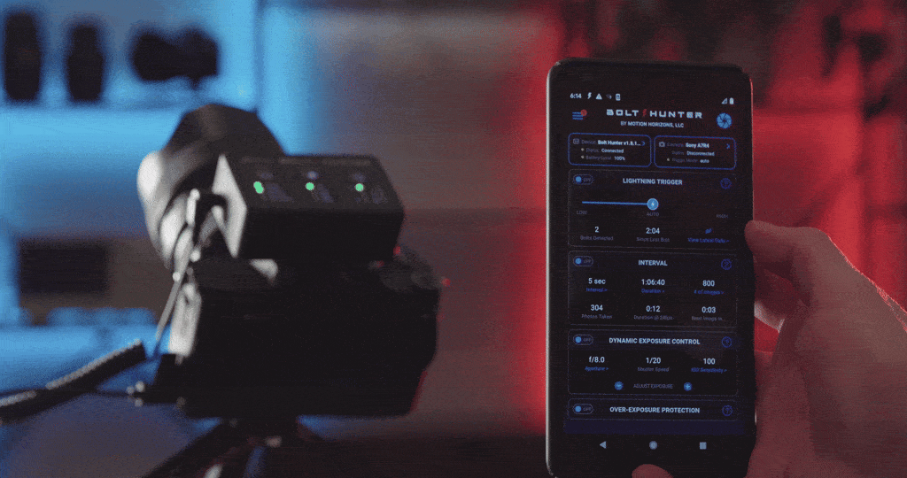 A person holding a smartphone displaying the Bolt Hunter app, with photography equipment on a tripod in the foreground, in a dark room with red and blue lighting.