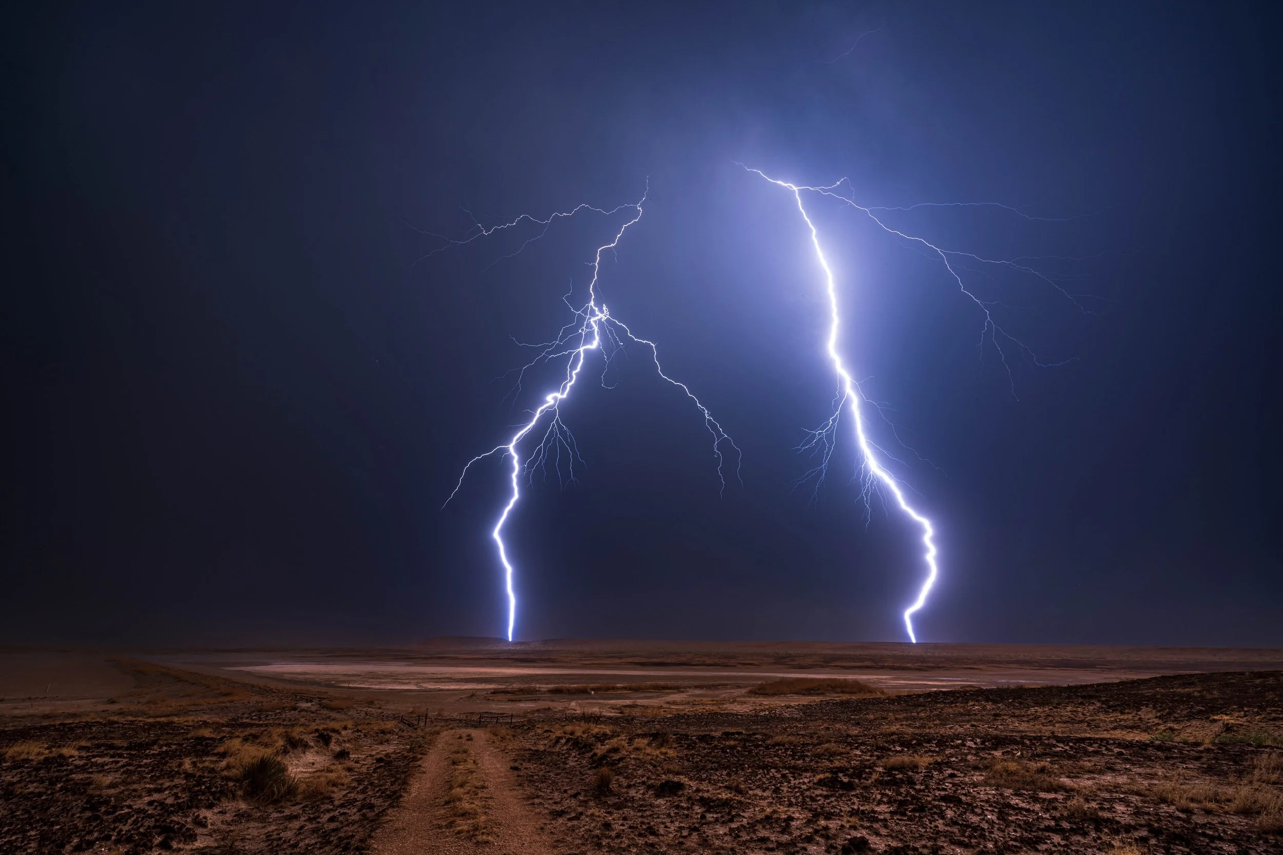 Lightning bolts striking the ground in a dark, cloudy sky over a barren landscape.