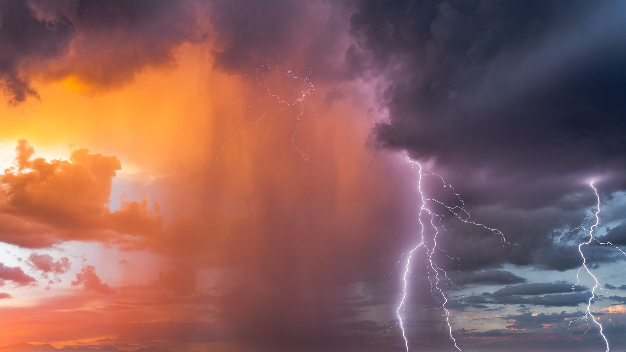 A lightning bolt beside an orange sunset and dark storm clouds