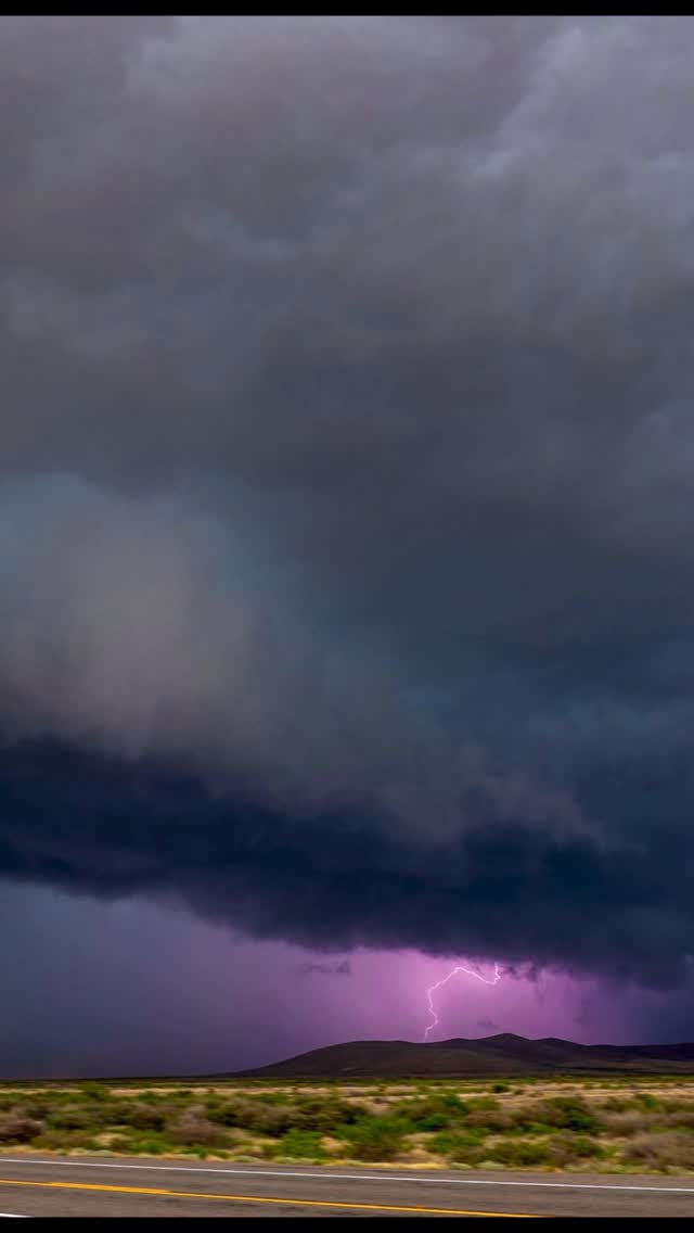 Lightning beneath a large storm cloud over a rural road