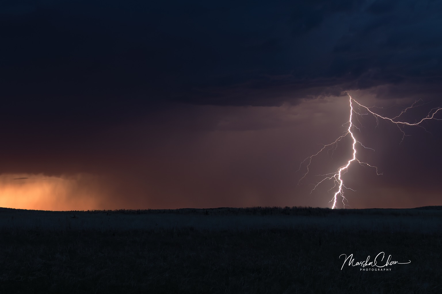 A lightning bolt above a dark sunset horizon