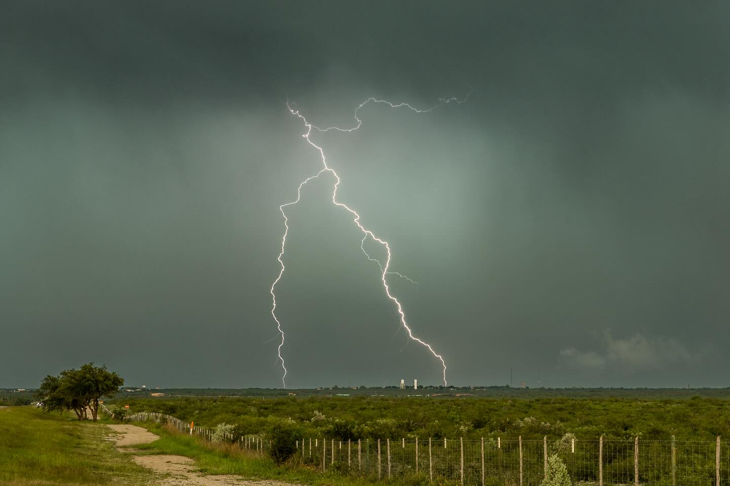 Lightning above a green field beneath storm clouds