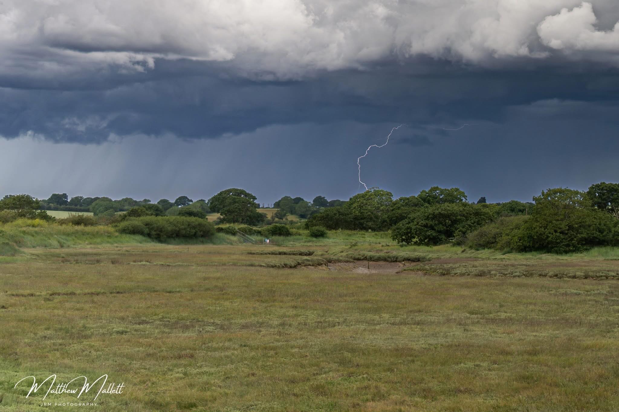 Lightning beneath dark clouds over green fields