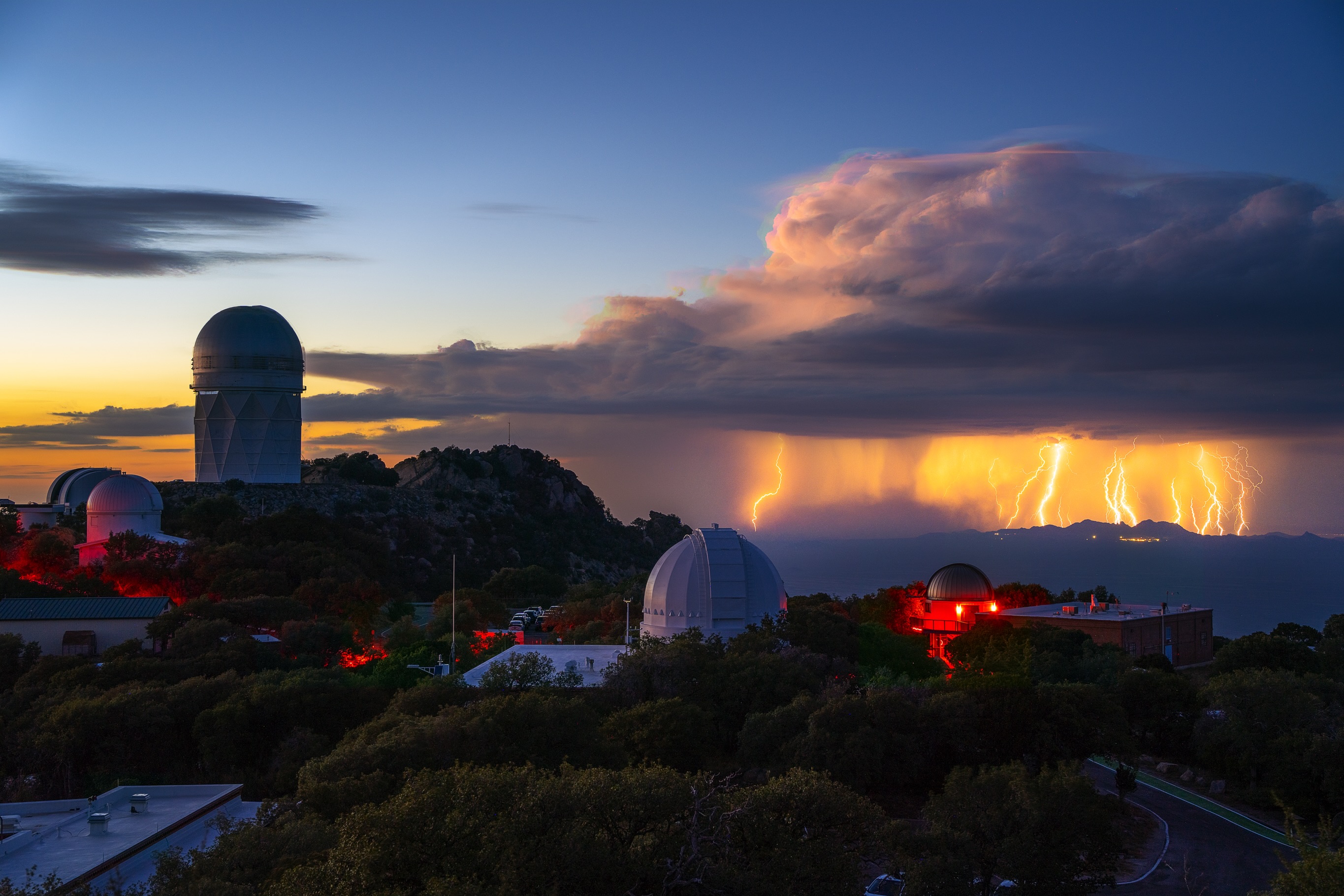 Distant lightning beyond observatory domes at sunset