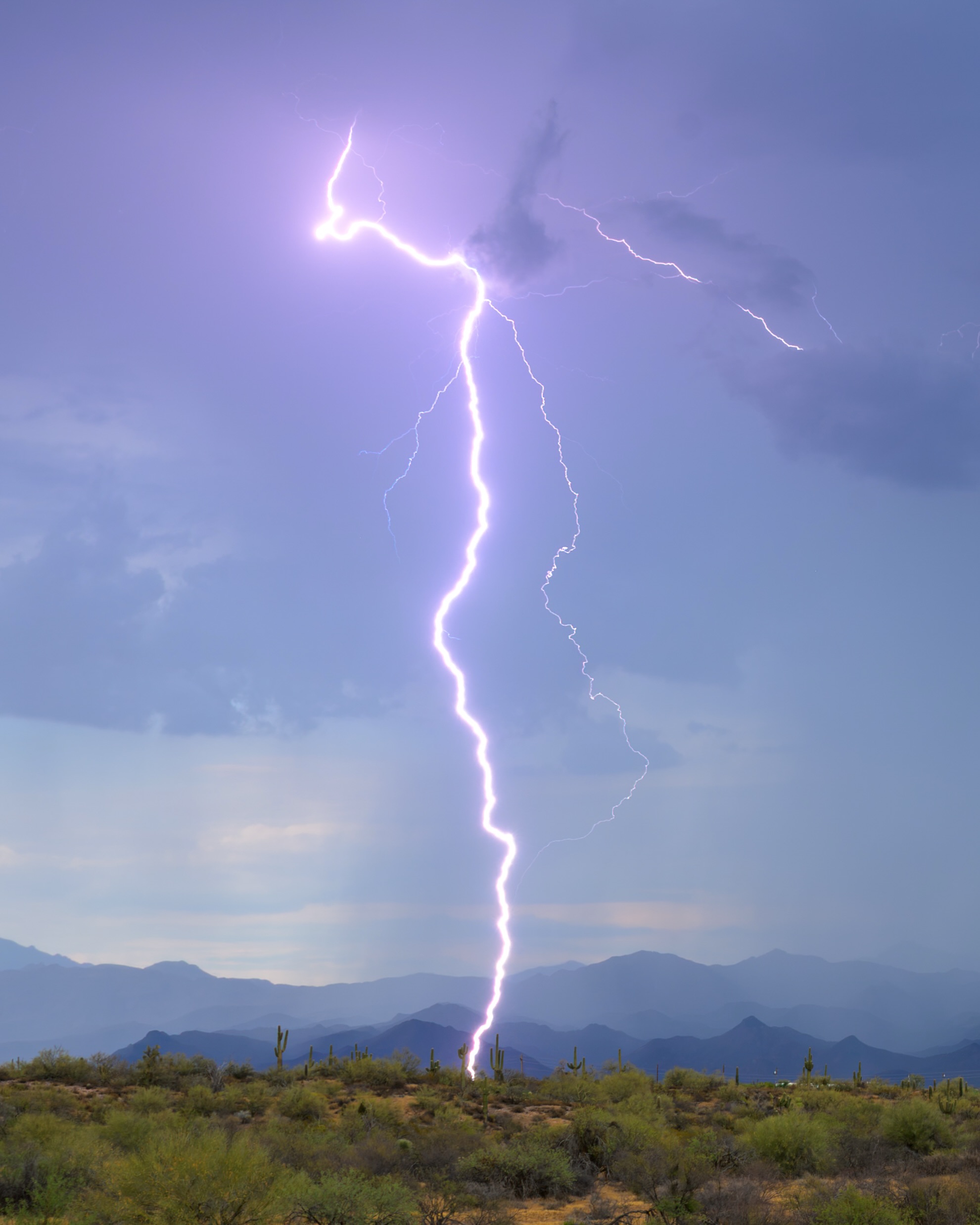 A bright daytime lightning bolt over desert mountains