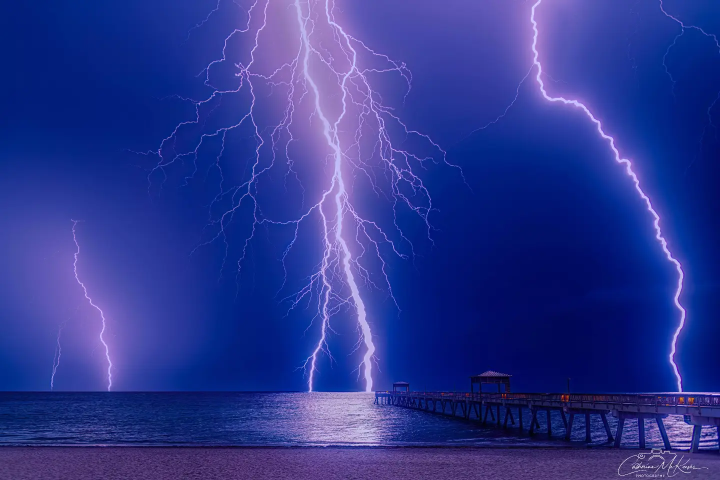 Multiple lightning bolts above the sea and pier