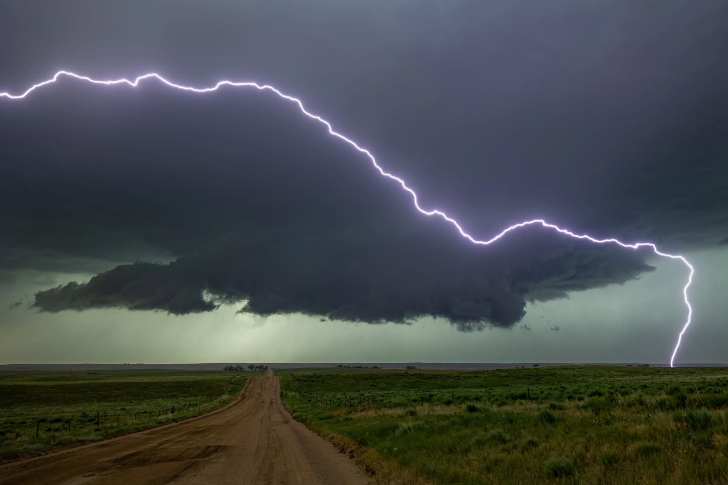 Lightning around a dark storm cloud above a country road