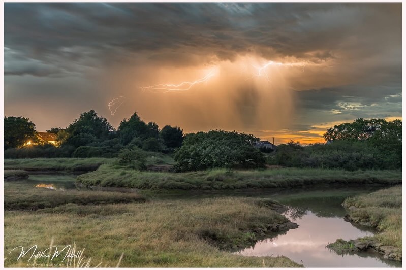Lightning in golden storm clouds above a wet landscape