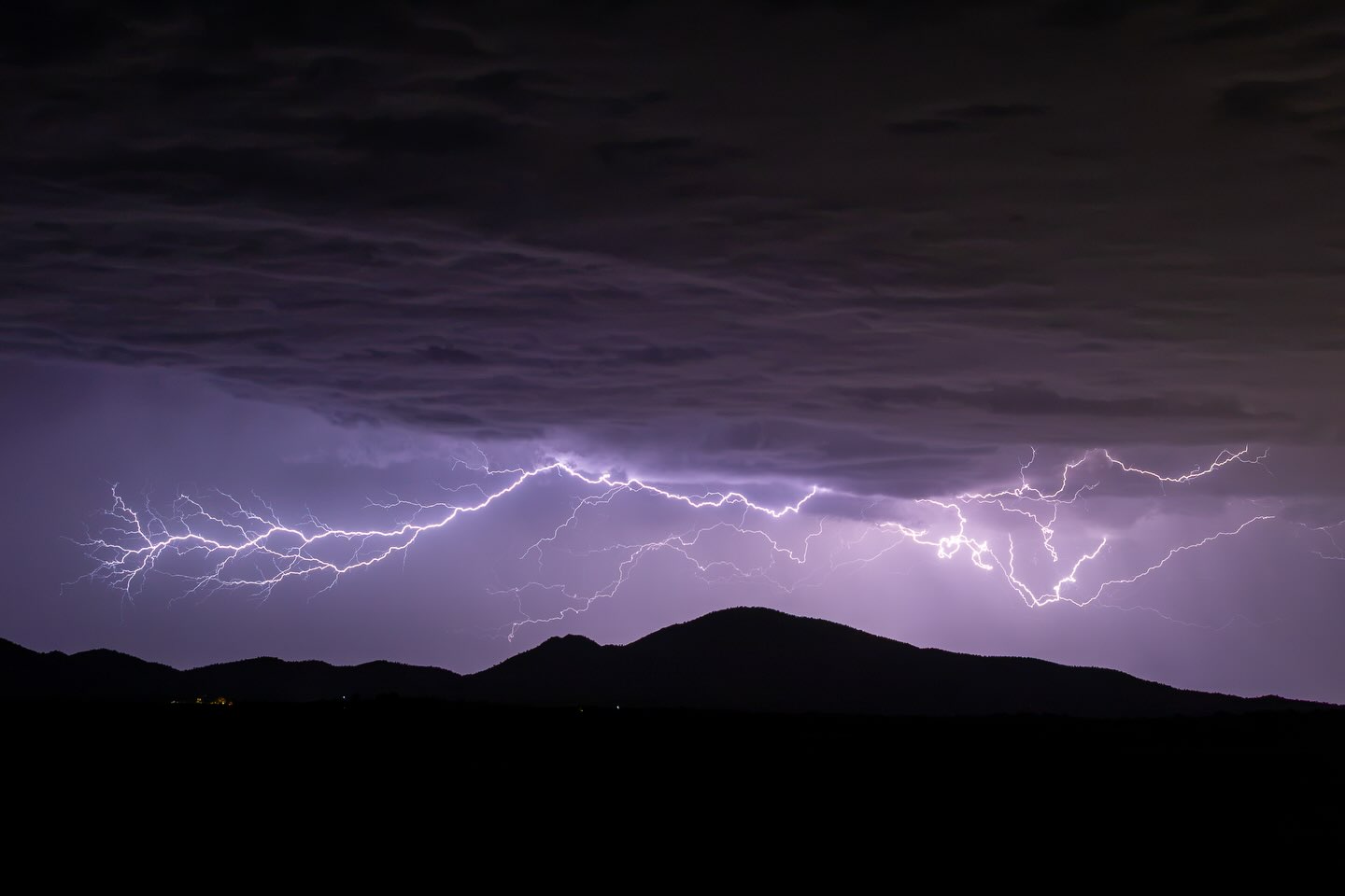 Lightning spreading across the sky above dark mountains